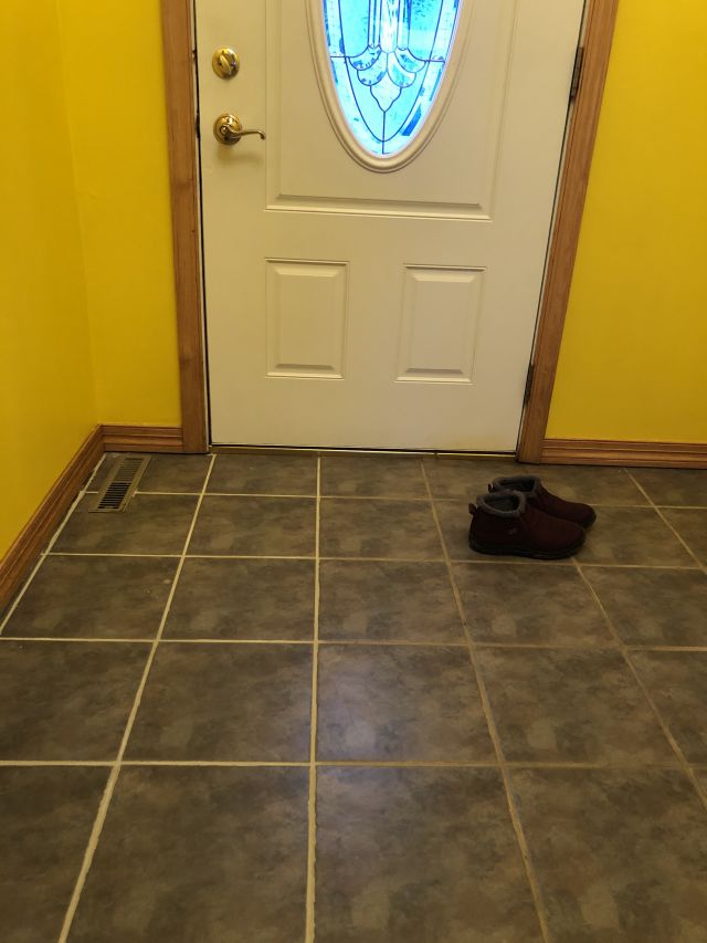 entryway of house with dark grey tiles, the left side shows bright white scrubbed grout, the right dirty