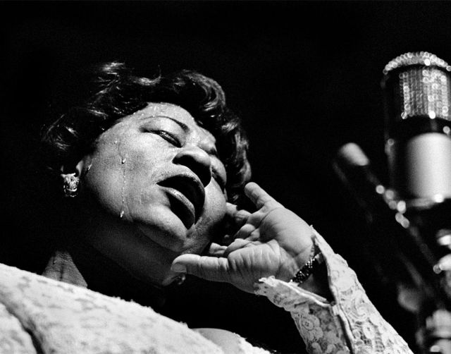 A Black woman at a microphone. She is sweating.
