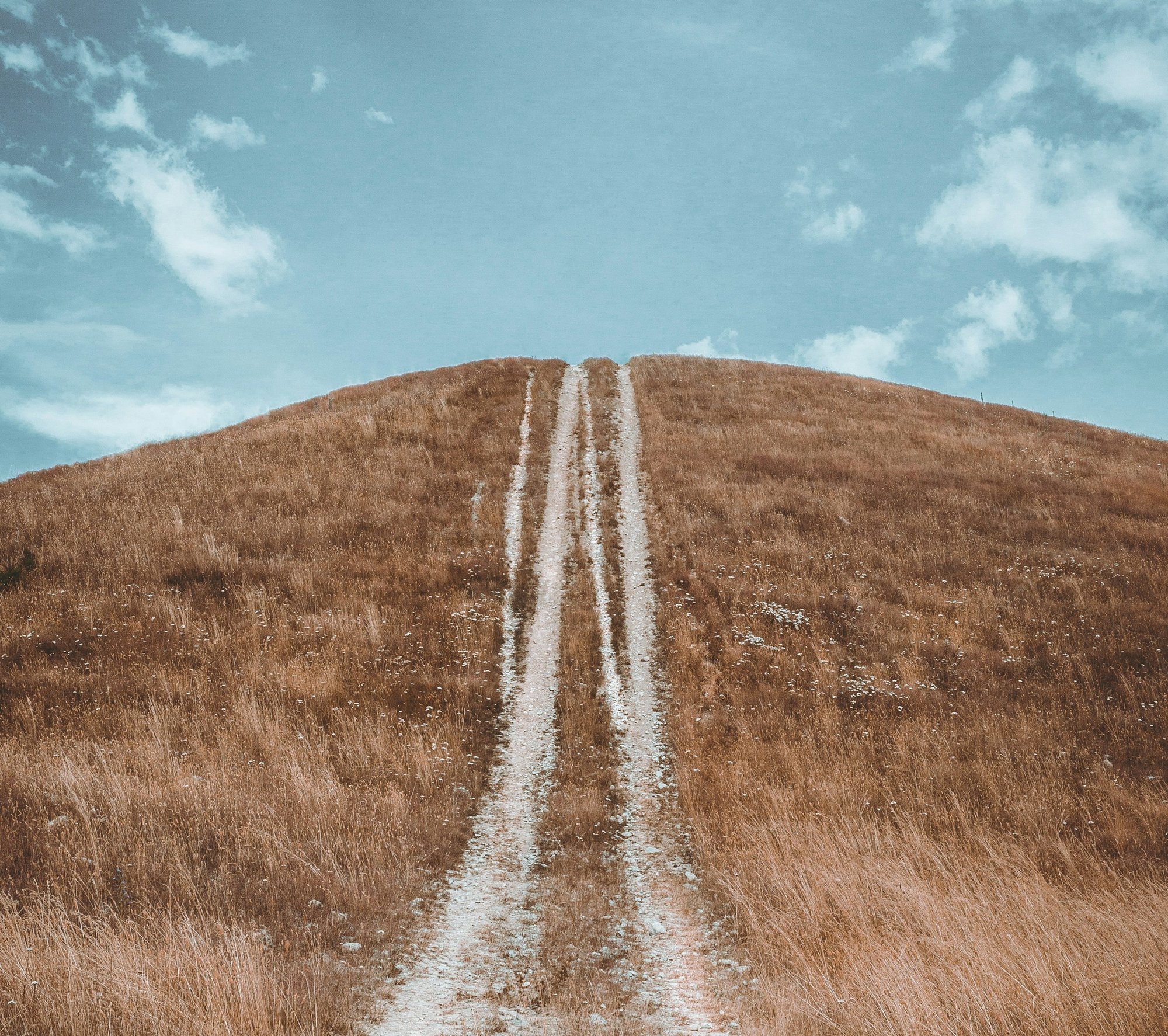 a dirt road going up a hill with a sky background