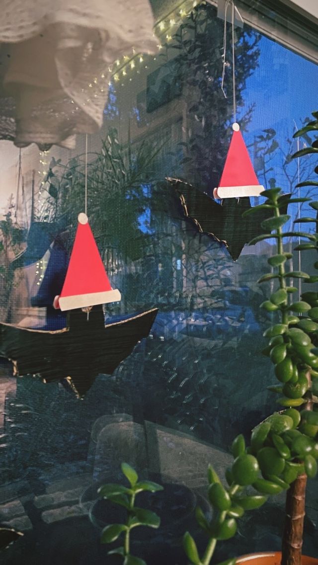 cardboard bats hanging from a window wearing little santa hats