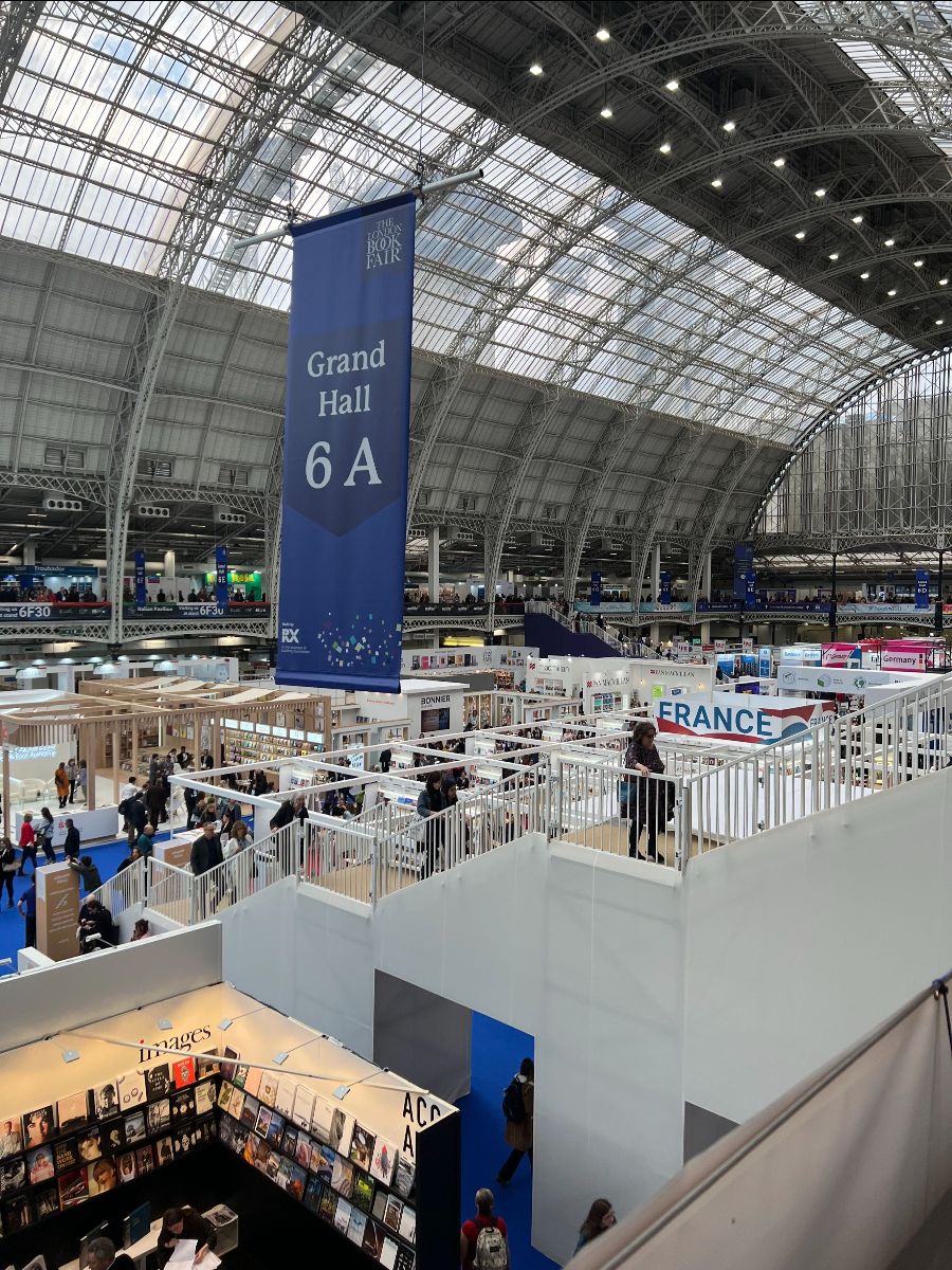 Photo from an upper floor of the London Book Fair 2023. There's a large convention hall packed with stands and booths.