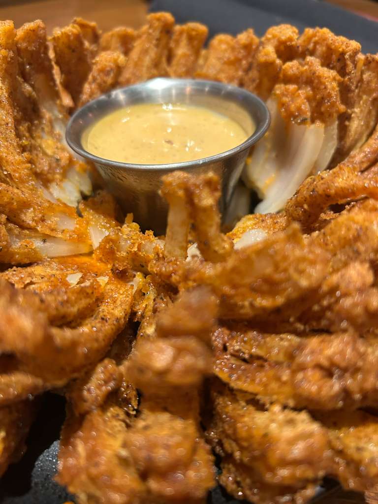 A close-up photo of a bloomin' onion with its sauce in the center.