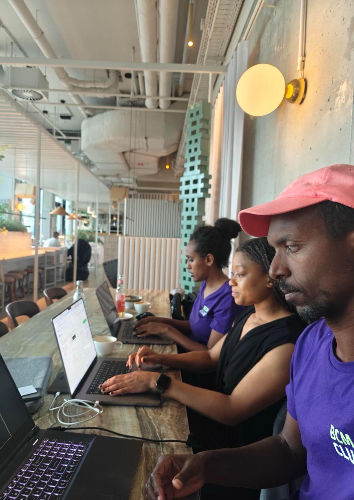 Photo of Saron, me, and Rob coworking at a long table, each sitting in front of our laptops.