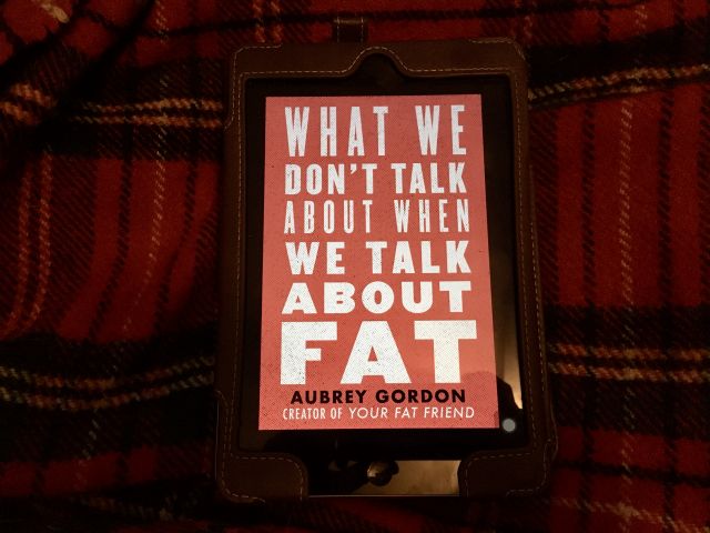 a photo of my iPad, resting on a red tartan blanket, showing the cover of  WHAT WE DON'T TALK ABOUT WHEN WE TALK ABOUT FAT by Aubrey Gordon