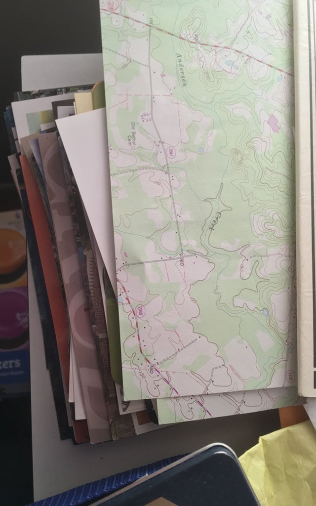 A shot of the postcards from above. They're obscured by a sheet of stationery that looks like a topographic map.