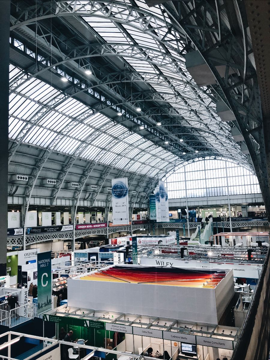 Screenshot of a large convention hall from a higher level looking down on a a series of exhibition stands.