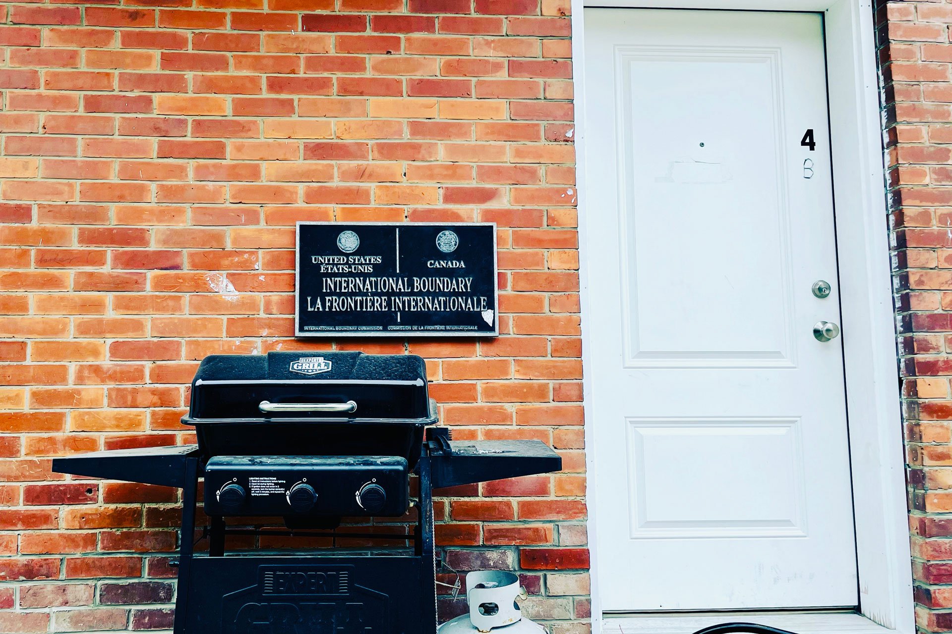 Photo of US-Canada border line sign on the side of a brick building