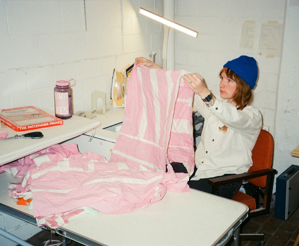 Cody is quilting a pink striped quilt and is wearing a blue hat