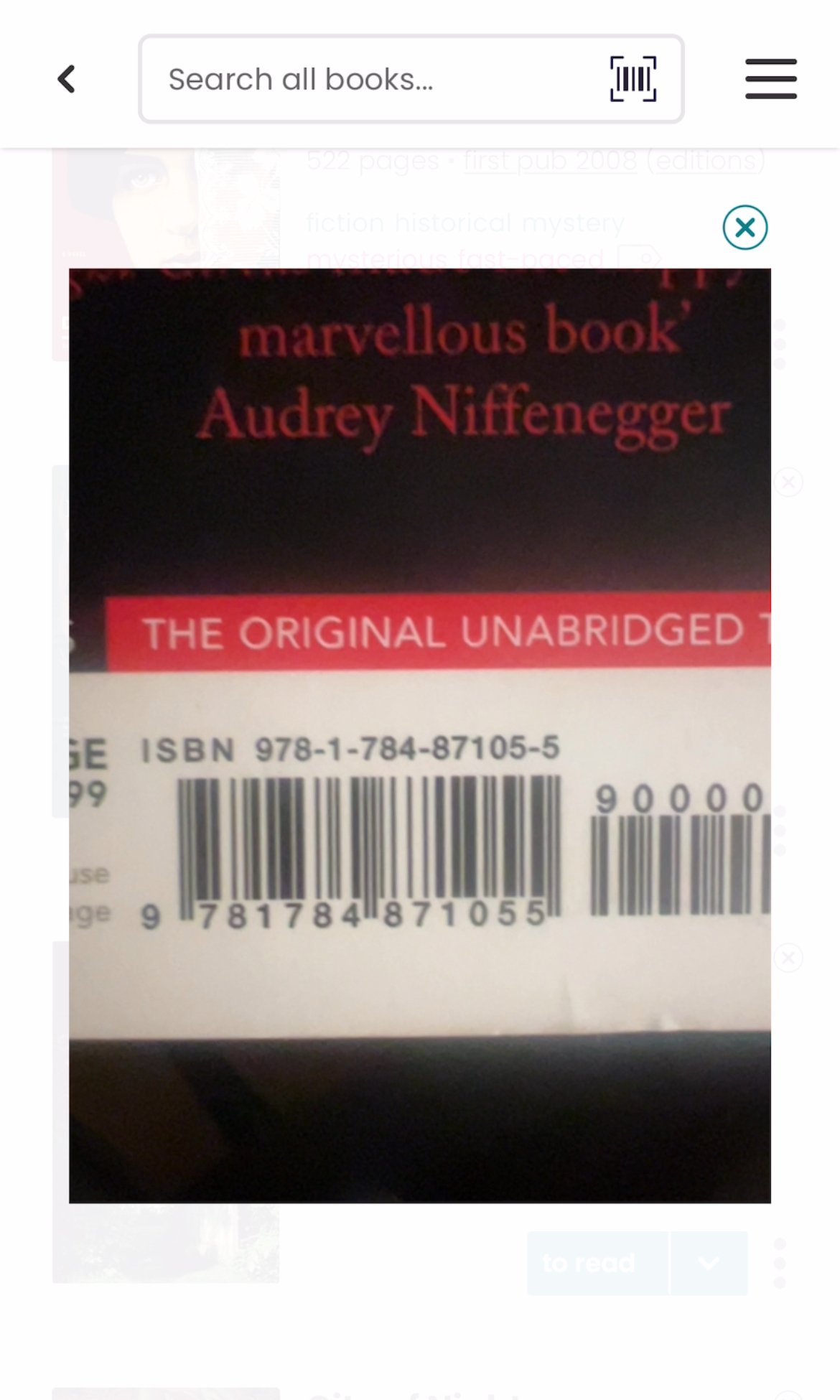 Screenshot of the The StoryGraph app. In the main search bar at the top, there's a small barcode scanner icon to the right. There's a camera view taking up the main body of the page and I've held up the back of a book, with its barcode, right up to the camera.