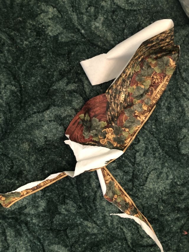 a ripped piece of wallpaper with green leaf and illustrated red and gold tapestries