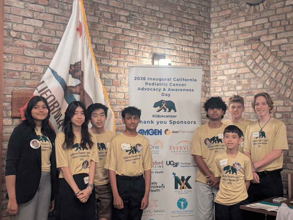 Group picture of the youth attendees at the California Pediatric Cancer Advocacy & Awareness Day next to the banner with logos of sponsors.