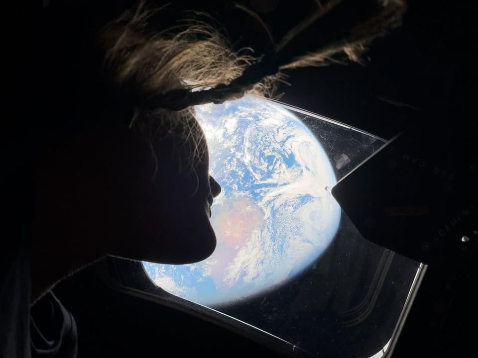 NASA astronaut and Artemis II mission specialist Christina Koch peers out of one of the Orion spacecraft's main cabin windows, looking back at Earth, as the crew travels towards the Moon.