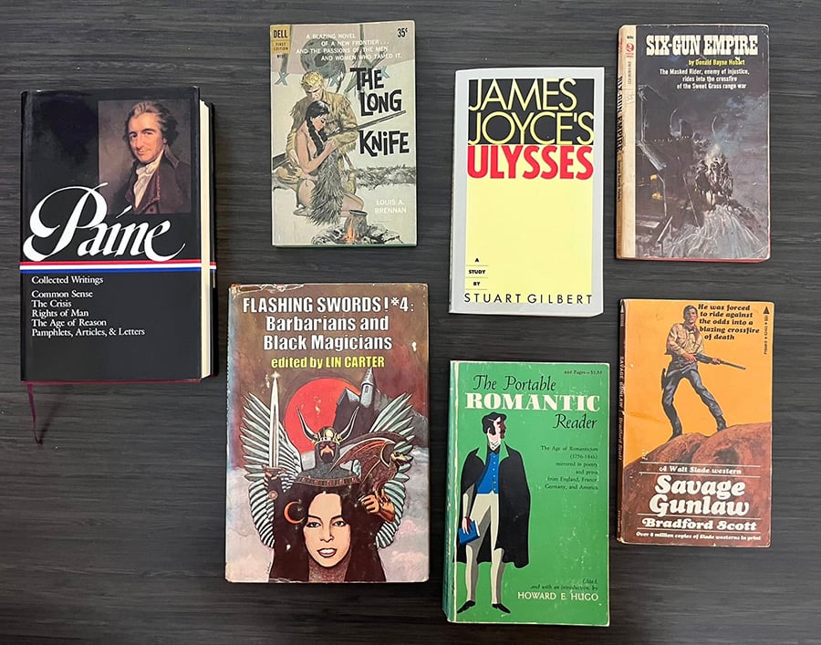 Seven books: Thomas Paine’s Collected Writings, a cheap paperback Western called The Long Knife, a Guide to James Joyce’s Ulysses, another cheap Western called Six-Gun Empire, a third cheap Western called Savage Gunlaw, The Portable Romantic Reader, and a hardcover, Flashing Swords #4: Barbarians and Black Magicians.