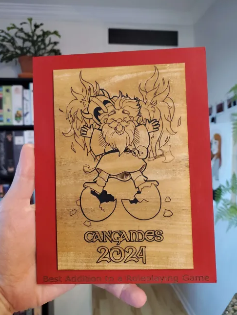 A plaque, held in hand, shows a laser-engraved rendition of a dwarf bursting from an egg. Text reads "Cangames 2024" and "Best Addition to a Roleplaying Game".