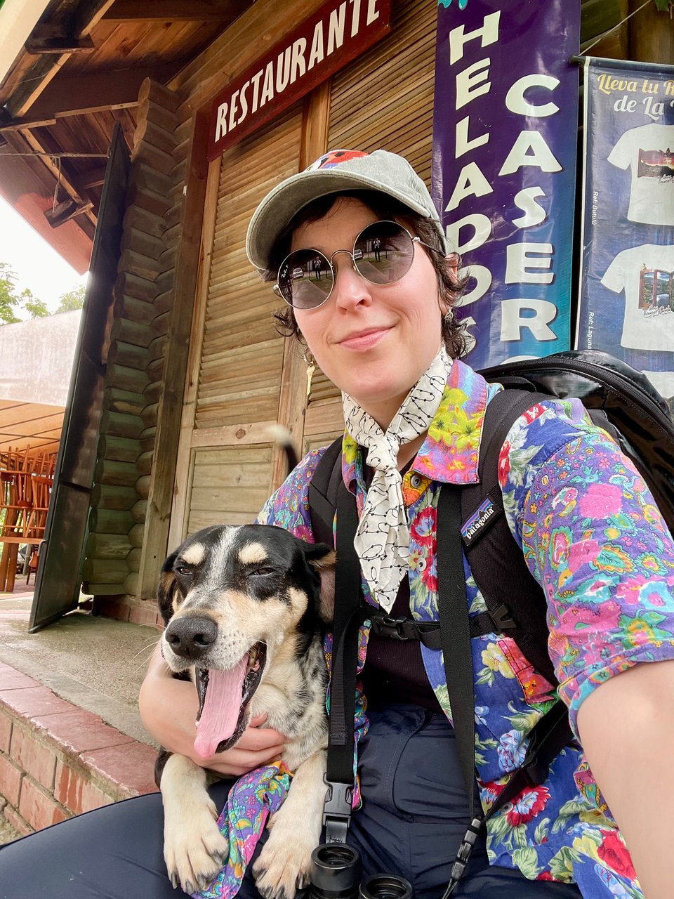 Me with sunglasses and a backpack in a national park with a brown and black dog yawning on my lap.