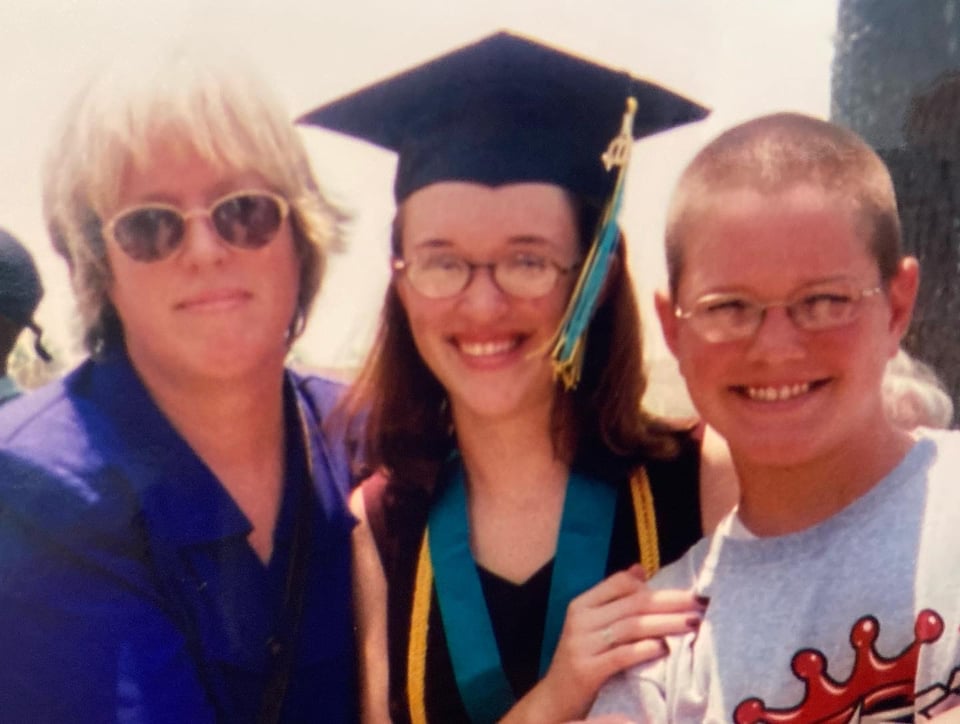 A scanned photograph of my mother, wearing a blue suit, me, wearing a graduation cap, a medal with a teal ribbon, and a gold graduation cord, and my brother, smiling and wearing a gray t-shirt. We are standing outside of the Ocean Center in Daytona Beach and I have my hand on my brother's shoulder.