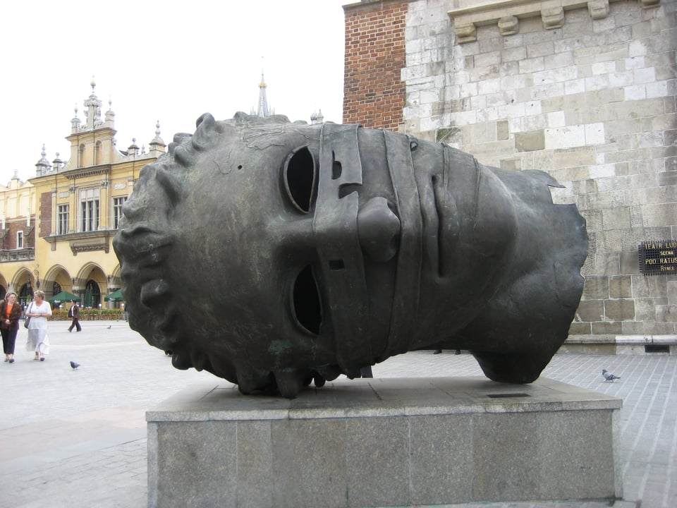 A sculpture of an extremely large severed head, lying on its side, with bandages across the nose and mouth.
