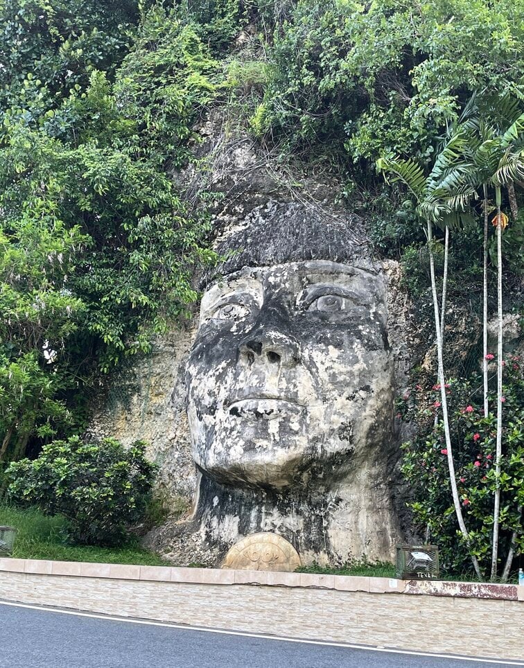 Sculpture of Cacique Mabodamaca embedded in limestone surrounded by greenery.