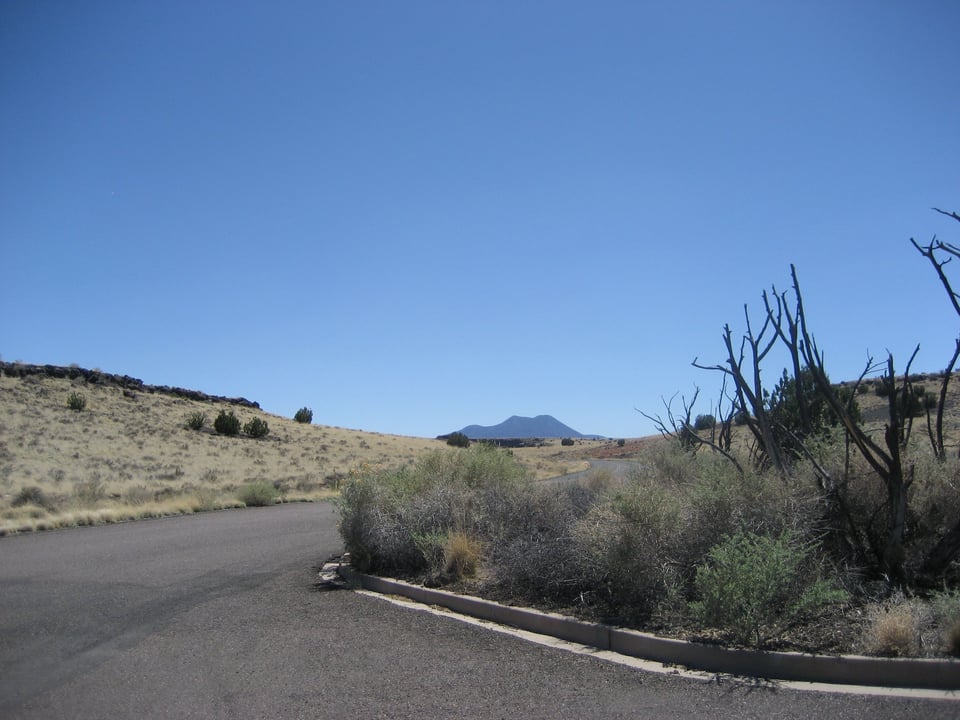 A paved road curves through a scrubby desert area, with a mountain in the distance.