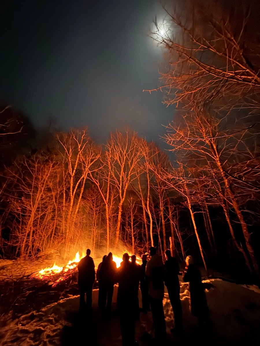 a group of people standing around a bonfire at night