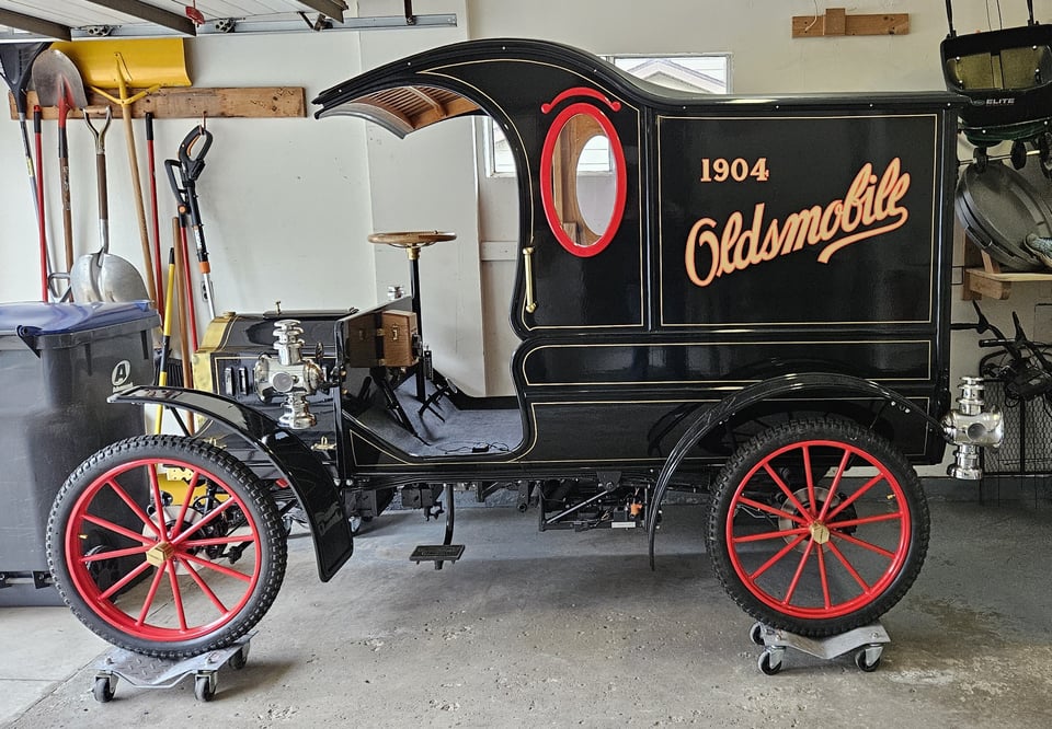 A shiny black "horseless carriage" with red accents that says 1904 Oldsmobile in gold lettering on the side.