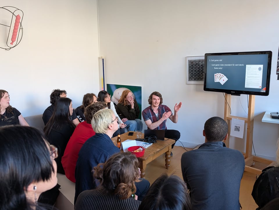 A man, crouching, points at a TV screen where his slides appear. An audience is listening in rapt attention.