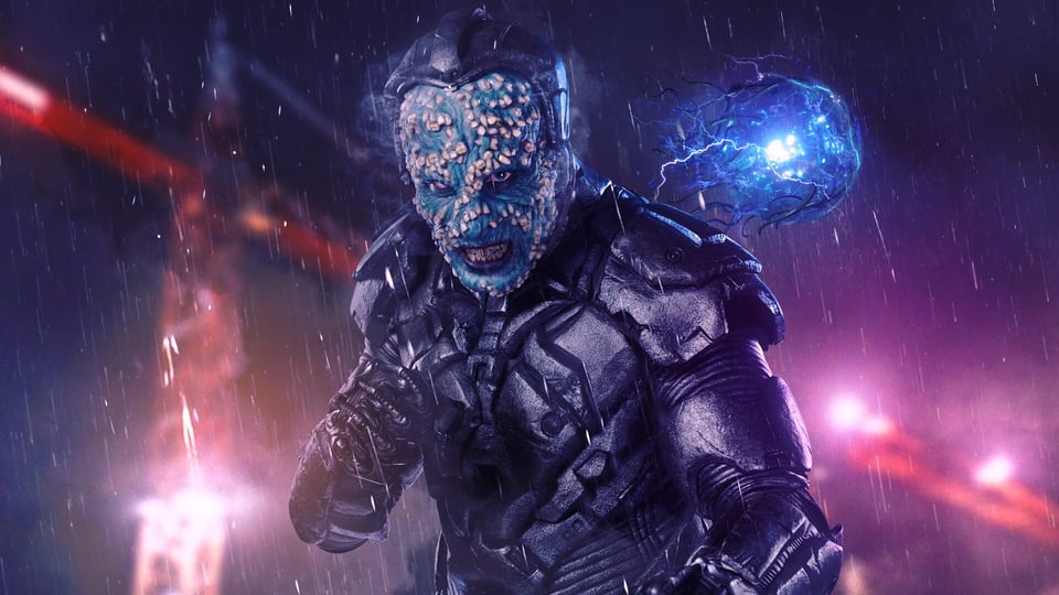 A snarling blue alien in power armor, numerous teeth stuck to his face; a blue wirey blob floats in the background.