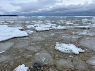 Lake Michigan lake water over rocks, with floating patches of ice under blue-white clouds