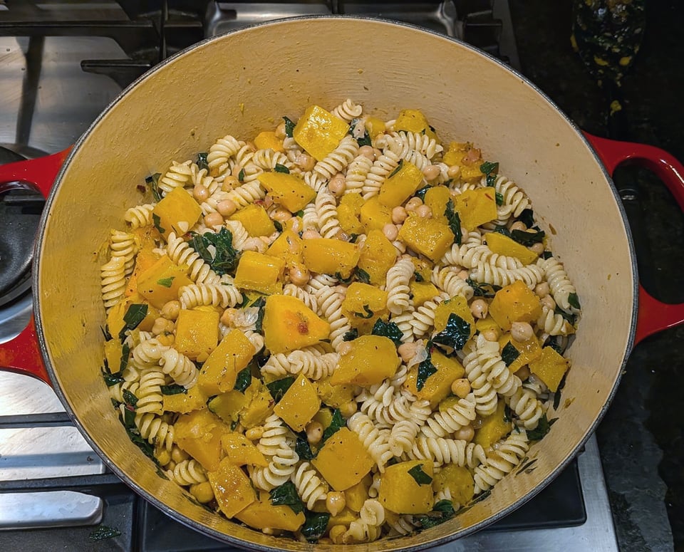 a dutch oven filled with rotini pasta, chunks of butternut squash, chickpeas, and shredded kale