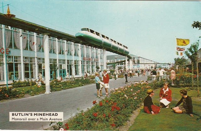 A postcard showing Butlin's in Minehead in the 1960s. There's a huge dining hall to one side of a main avenue, and roses and lawns on the other. And running overhead is a monorail.