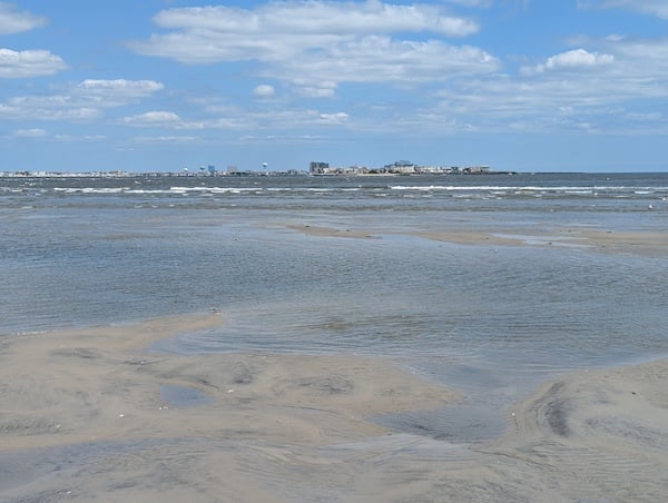 A beach at low tide, with water pooling into depressions in the sand; beyond the beach, an ocean with waves, and on the other side of the water, the tall buildings of Atlantic City