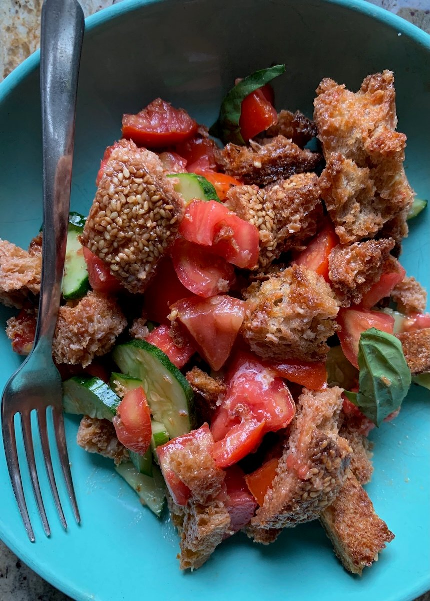 A salad of croutons, tomatoes, cucumbers and basil in a blue bowl