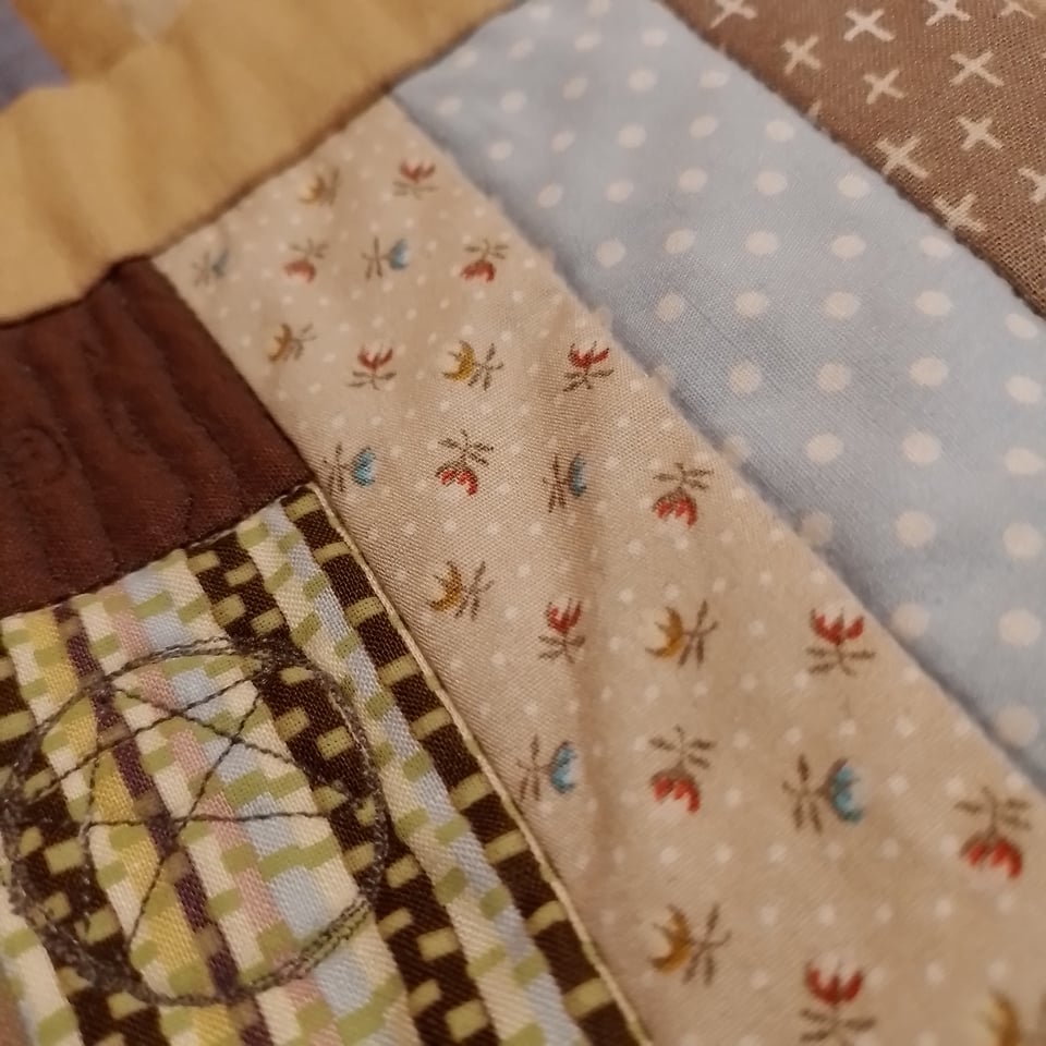 Close-up of a patchwork quilt, including floral and polka dot strips, and an embroidered five-pointed star