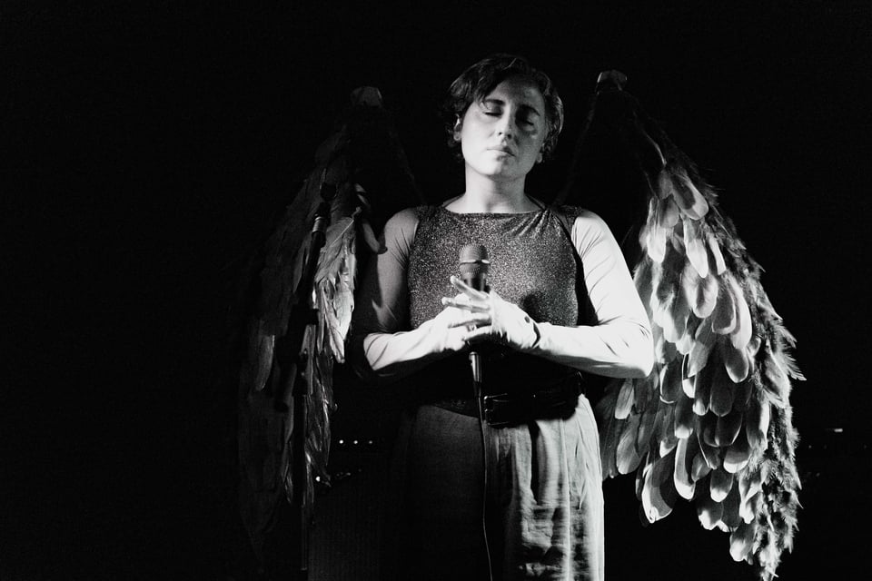 a black and white shot of artist jasper jones in a quiet moment of a song, holding the mic with eyes closed, incredible angel wings visible behind them