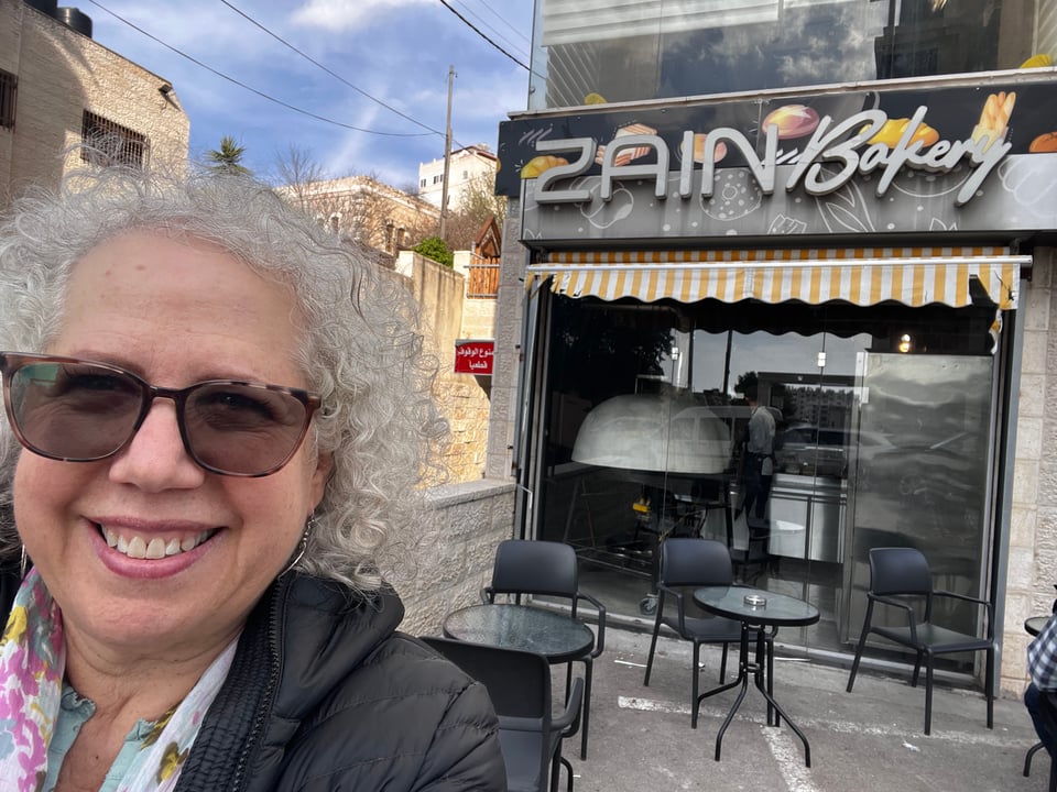 Nancy smiling in front of a small storefront with the sign Zain Bakery