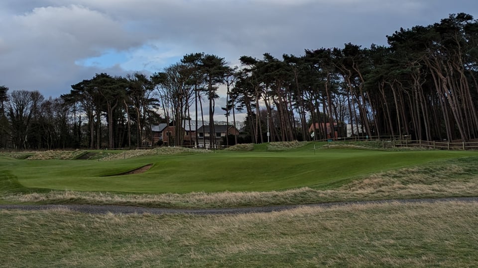 Formby 16th raised green, vast greenside bunker at the front, pines and expensive houses behind