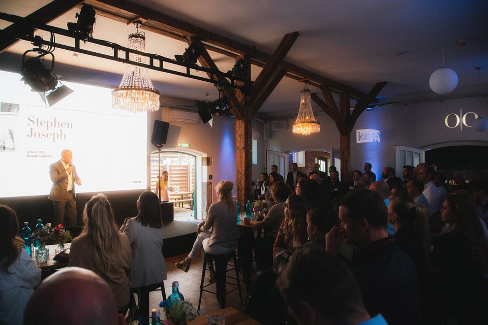 Bild vom inneren des Glasvoll zeigt eine Bühne mit einer Person die vor vielen interessierten Zuhörern spricht