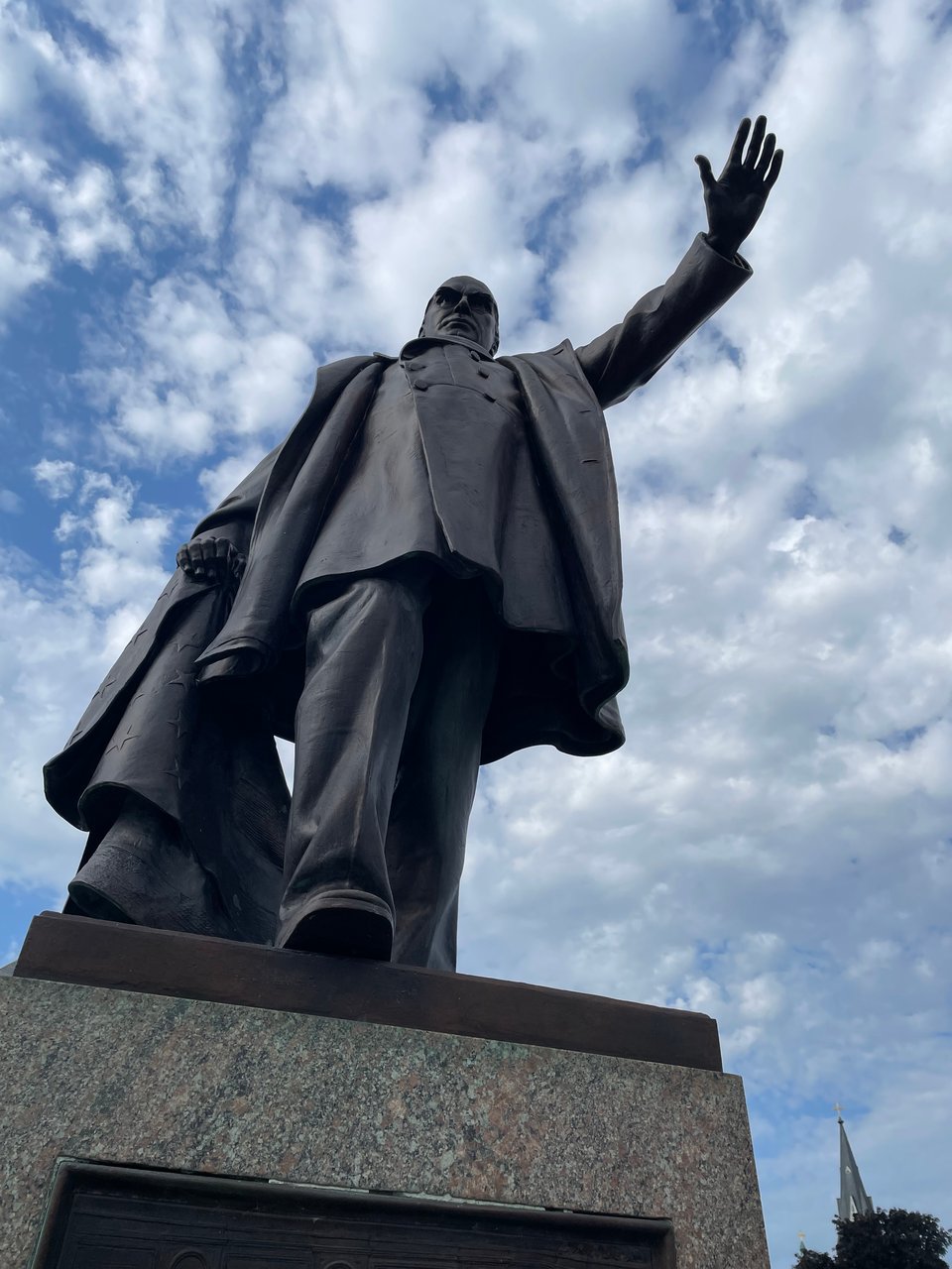 Looking up at McKinley from the pedestal, he is scowling and holding his hand out against a blue sky with some clouds