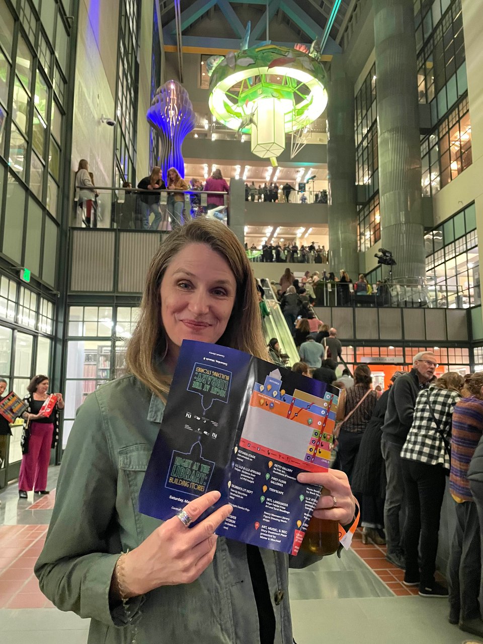A woman smiles and holds a program in a tall, multi-story atrium