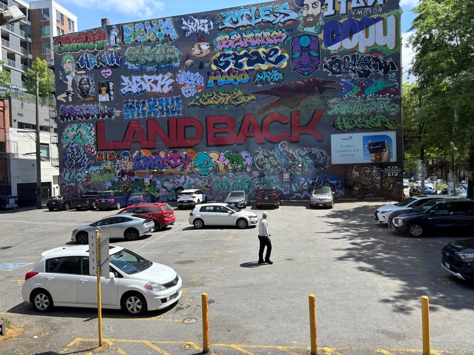 A wall of a building in Vancouver with "LAND BACK" prominent in capital red letters, graffiti art surrounding it.