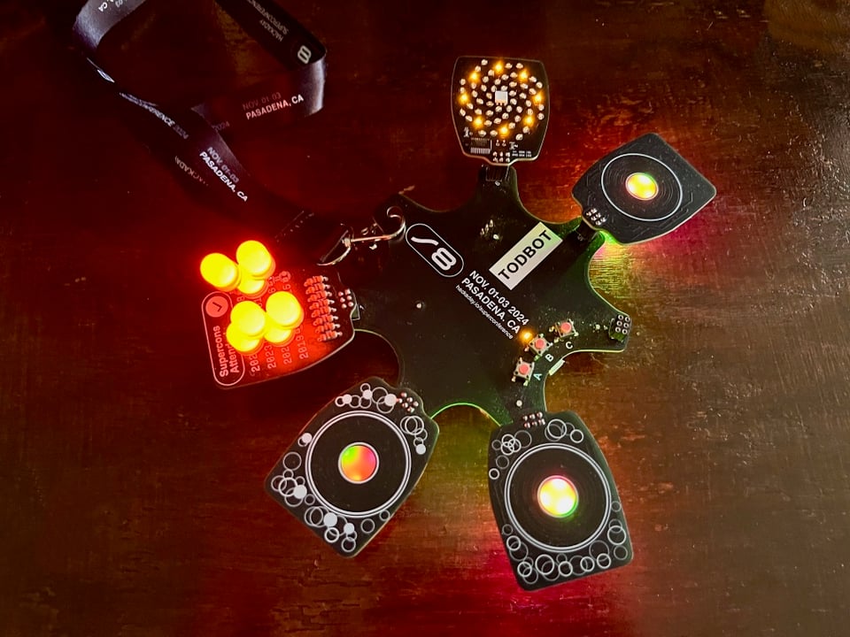 Supercon 2024 badge which features six connectors for add-ons. This badge has 3 cap touch add-ons and two LED add-ons