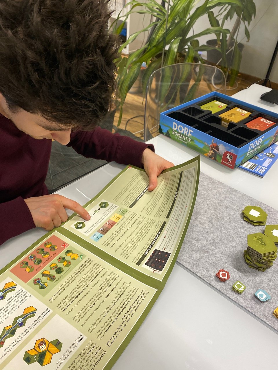 One person sitting in a meeting room, intently studying the board game instruction manual for “Dorfromantik”