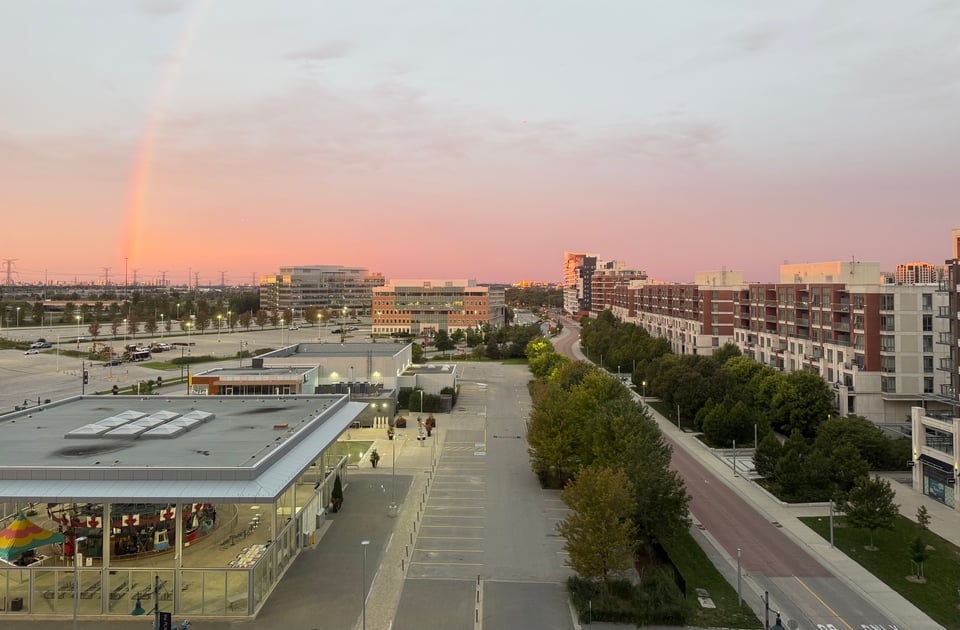 photo of Downtown Markham, ONT from a hotel room window on the 7th floor; it's early morning and the sky is pink, with a rainbow off to the left side.