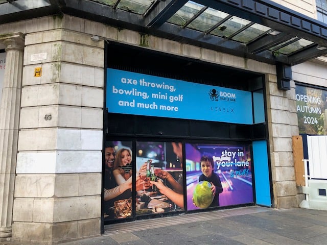 Sign on a light stone building in downtown Glasgow advertising: "axe throwing, bowling, mini golf and much more"