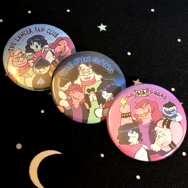 A photo of three unofficial Deltarune buttons lined up diagonally. They are “The Lancer Fan Club,” “The Fun Gang,” and “The $!$! Squad.” They all feature Kris, Susie, Ralsei, and Lancer in different compositions.
