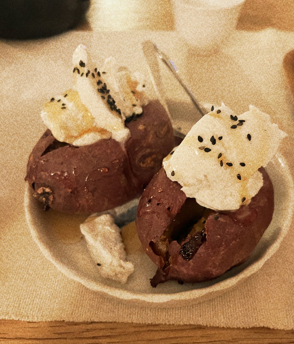 a picture of two sweet potato sundaes; two roasted sweet potatoes, with vanilla ice cream, black sesame seeds, and brown sugar syrup on top, on top of a small plate.