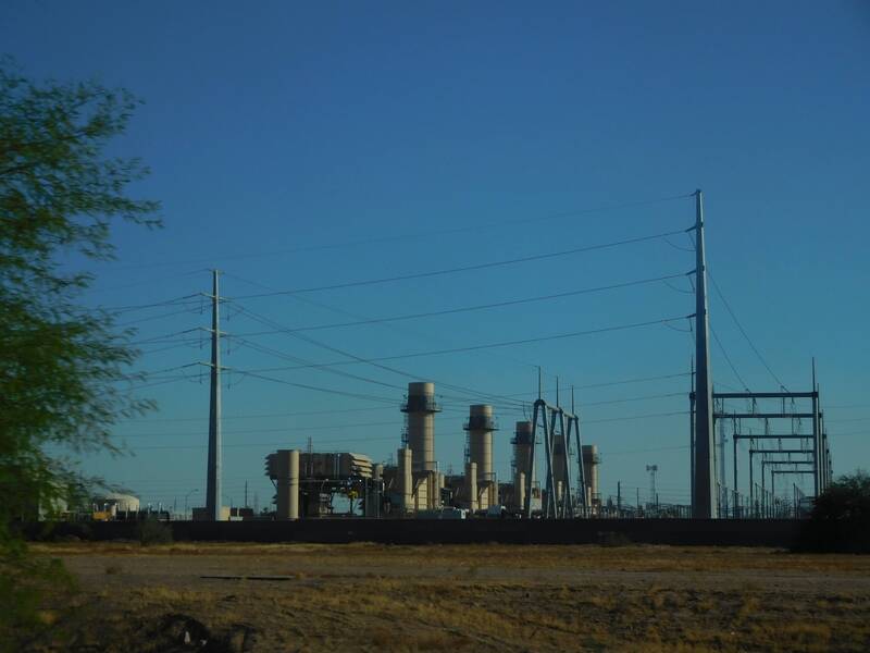 A power station with big cylindrical structures flanked by huge, pole-shaped transmission towers.