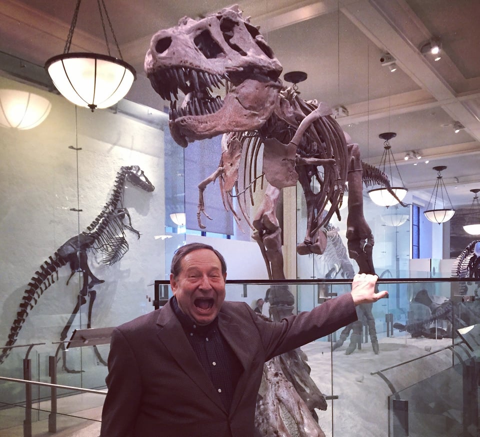 Man pretending to roar while standing under Tyrannosaurus Rex skeleton at Museum Of Natural History, NYC