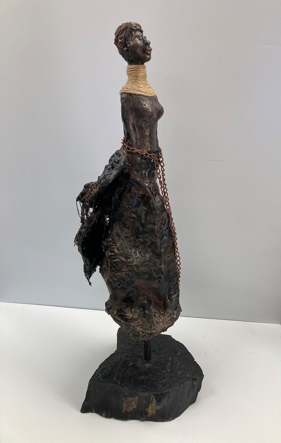 An encaustic sculpture of a short-haired woman with african descent, with a chain draped around her midsection. She is looking up, with a hopeful and determined expression.
