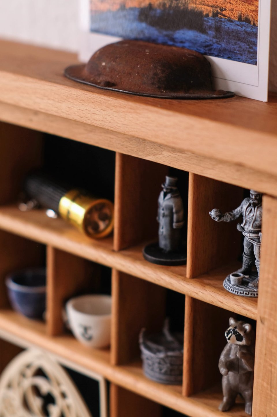 Photo close-up of the compartments and the trinkets inside. Two miniature teacups and grey RPG figurines. The upper edge of the shelf and the drawer handle, still rusty, is seen at the top.